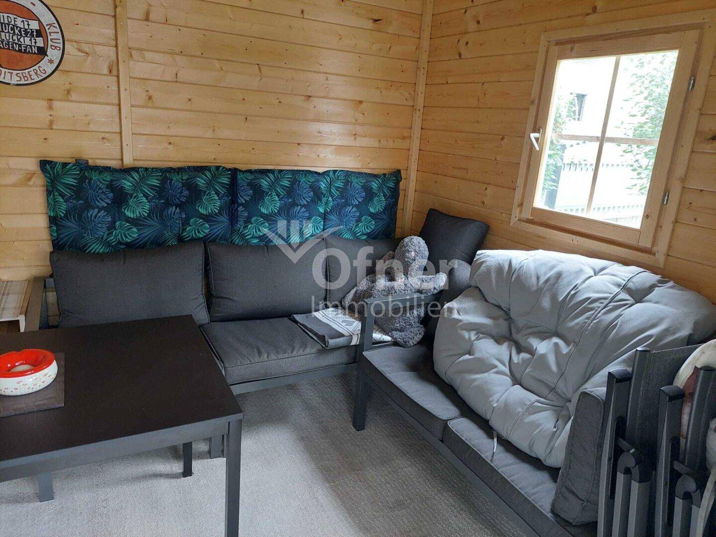 Innenansicht eines Gartenhauses mit Holzverkleidung und bequemen Sofas.