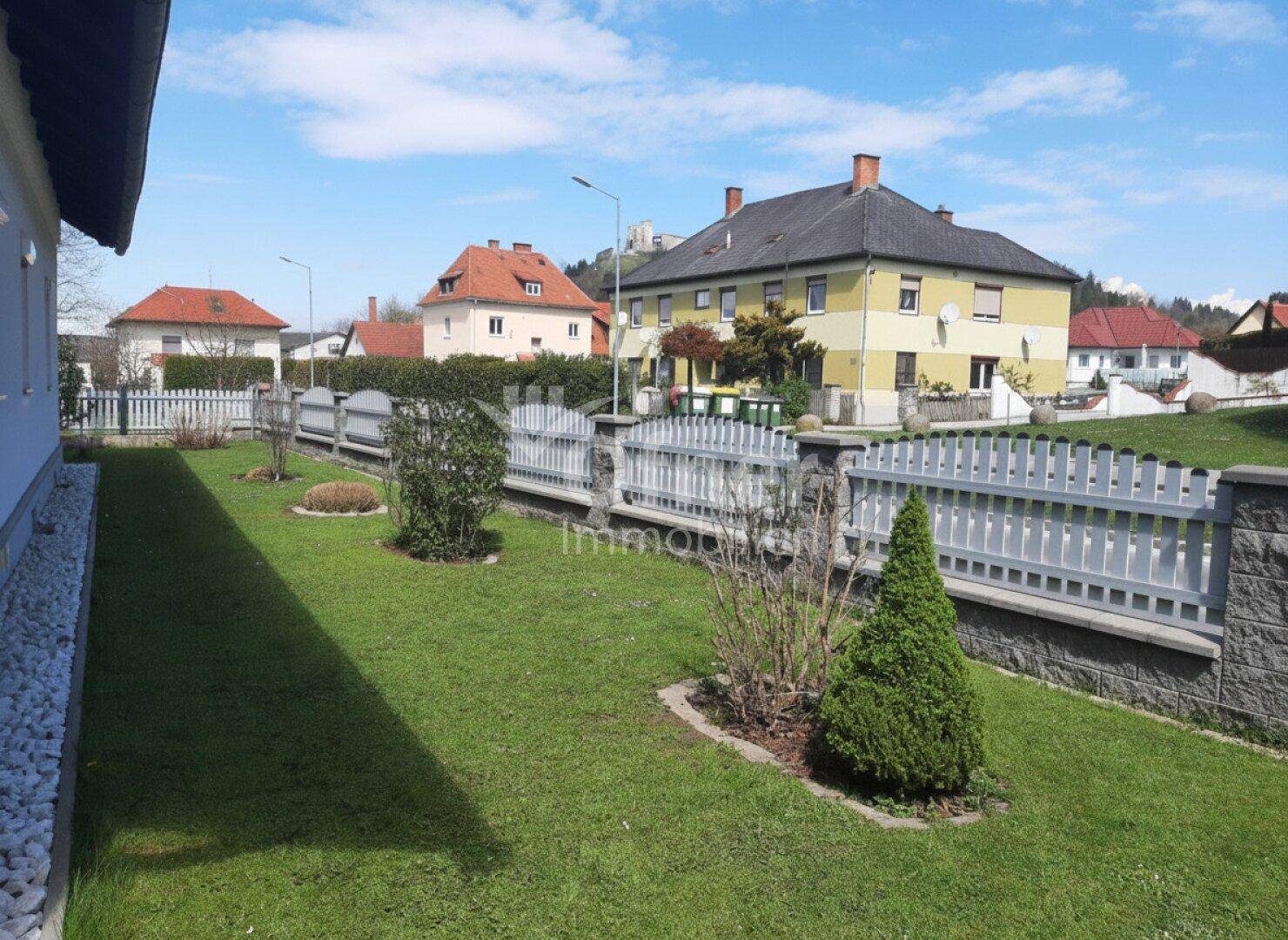 Gepflegter Gartenbereich mit Rasenfläche und weißem Zaun, umgeben von Wohnhäusern.