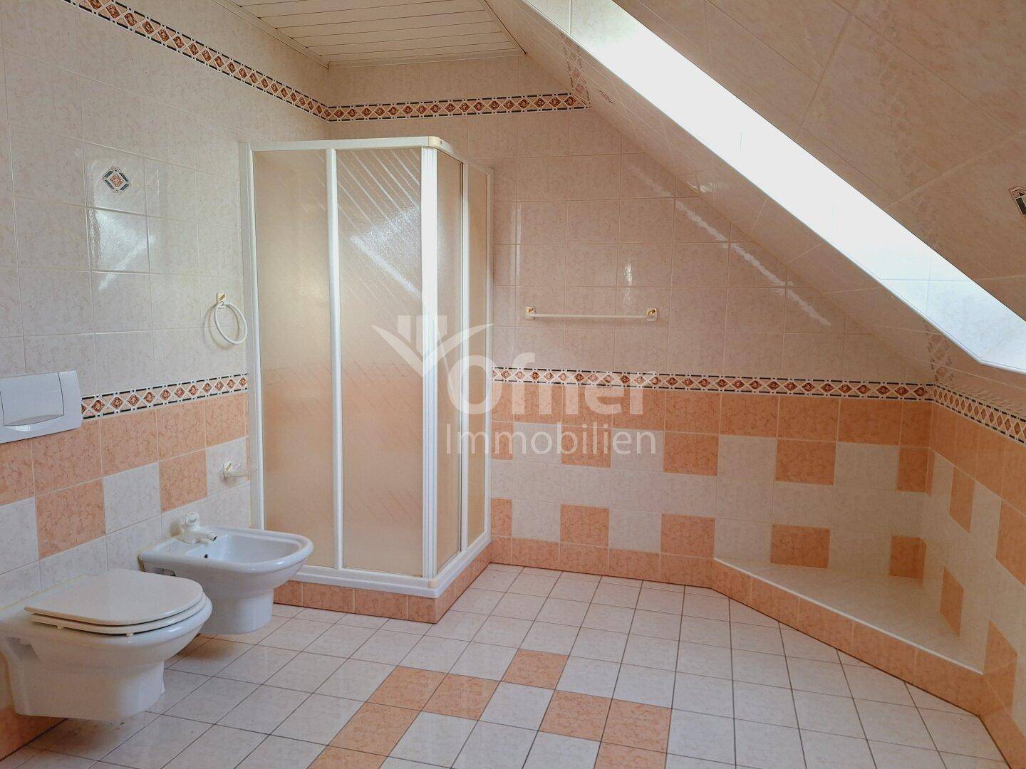 Badezimmer im Dachgeschoss mit Duschkabine, Bidet und Fliesen in warmen Farbtönen.