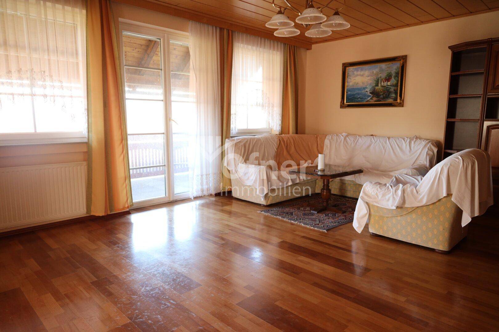 Helles Wohnzimmer mit Holzboden und Zugang zu einem Balkon, ausgestattet mit bequemen Sofas.