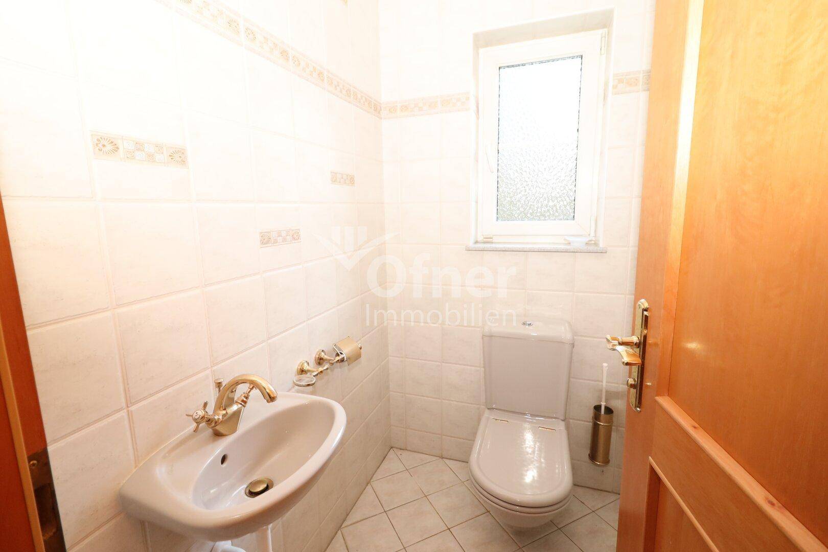Gäste-WC mit Fliesen an Wänden und Boden, ausgestattet mit Toilette und Waschbecken.