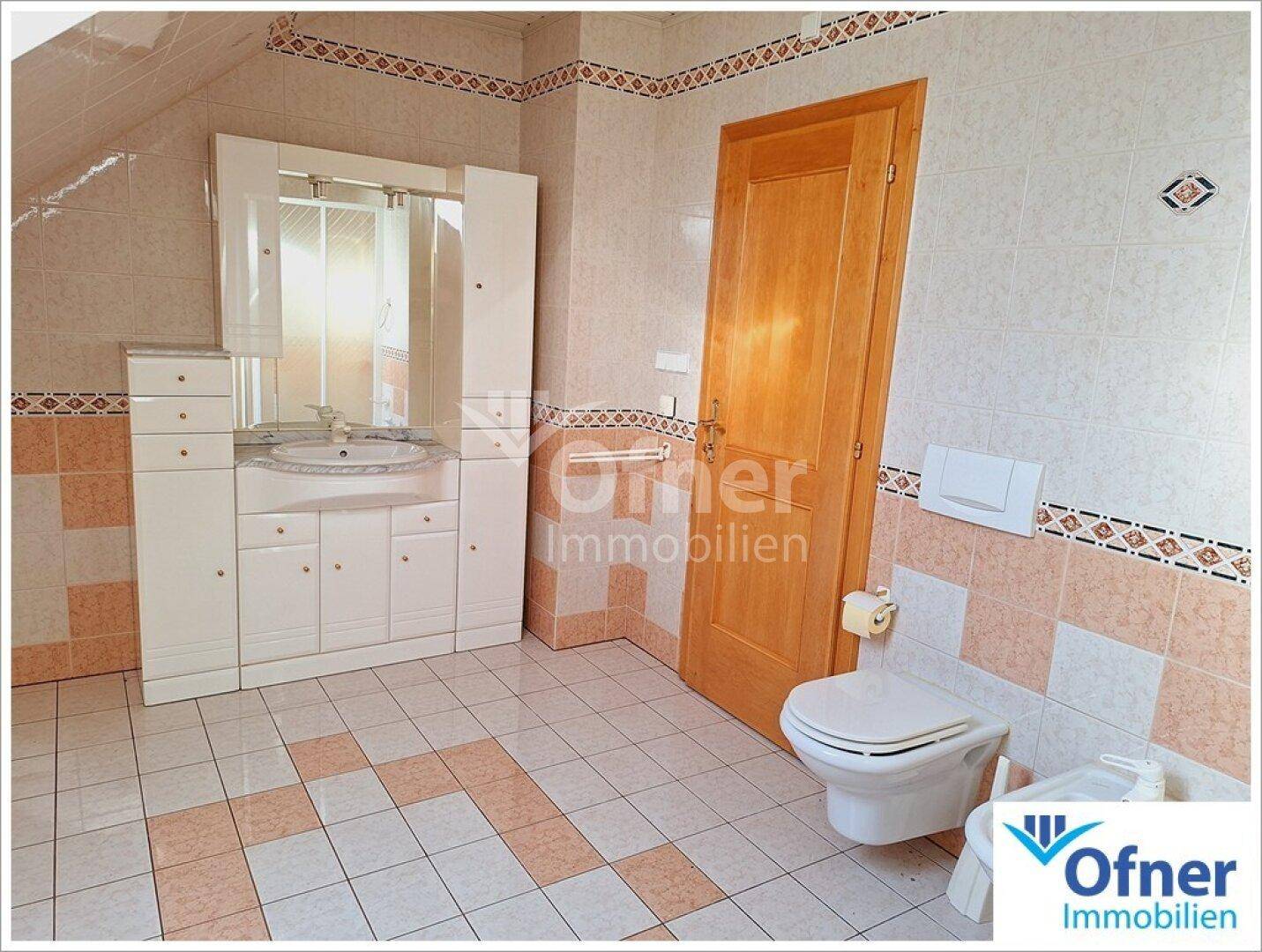 Badezimmer im Dachgeschoss mit Fliesenboden, Waschbecken und Toilette, in hellen Farben.