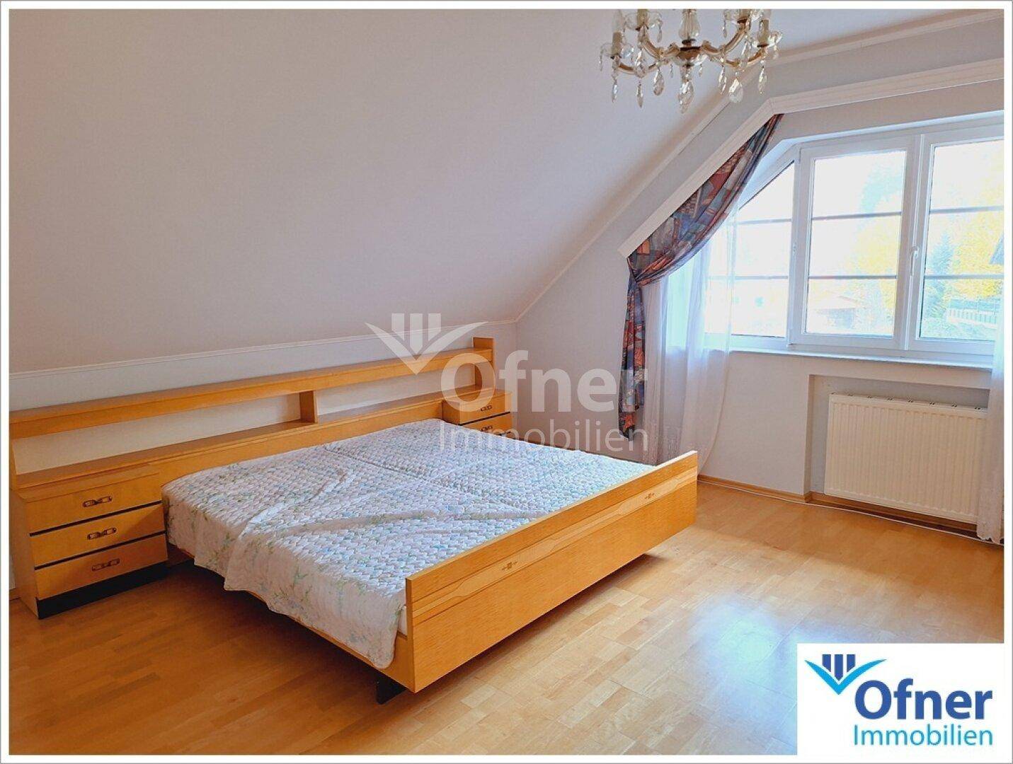 Helles Schlafzimmer im Dachgeschoss mit Holzboden, Doppelbett und Dachschrägen.