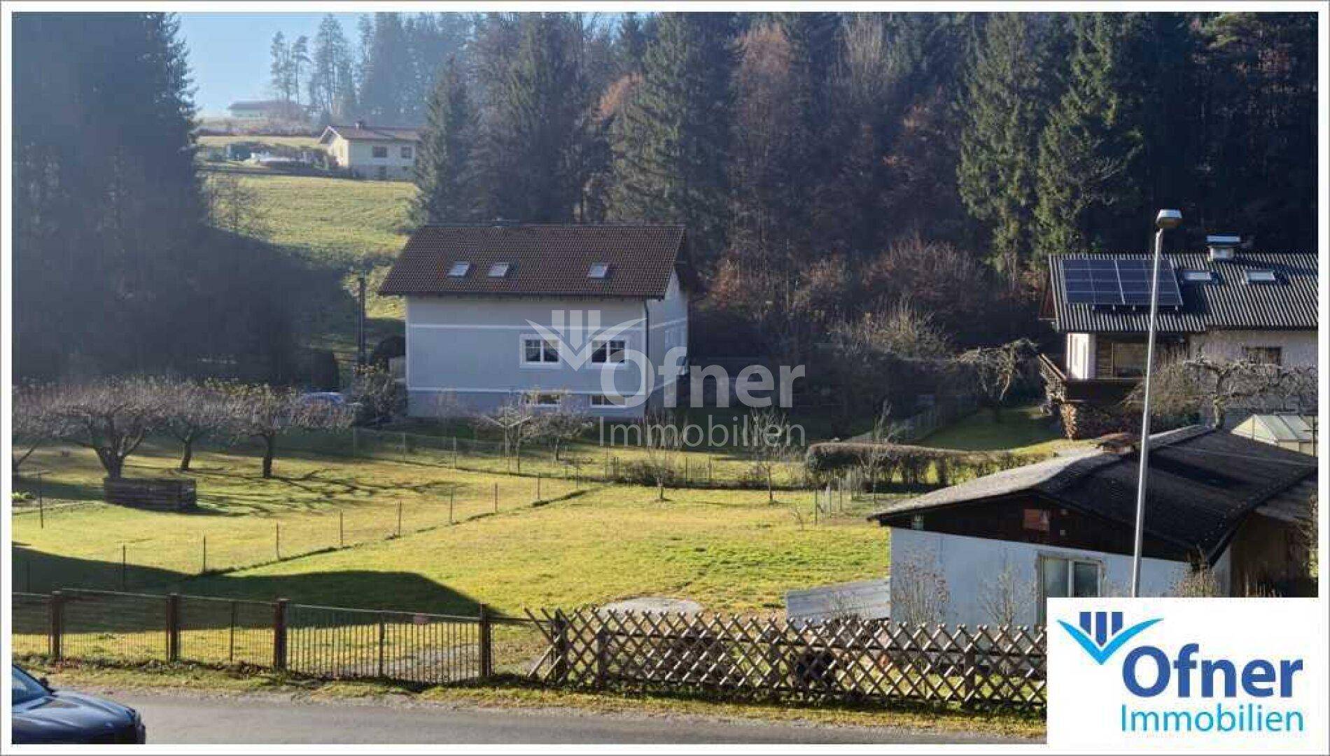 Panoramablick auf ländliche Wohnhäuser mit grünen Feldern und Wald im Hintergrund an einem sonnigen Tag.