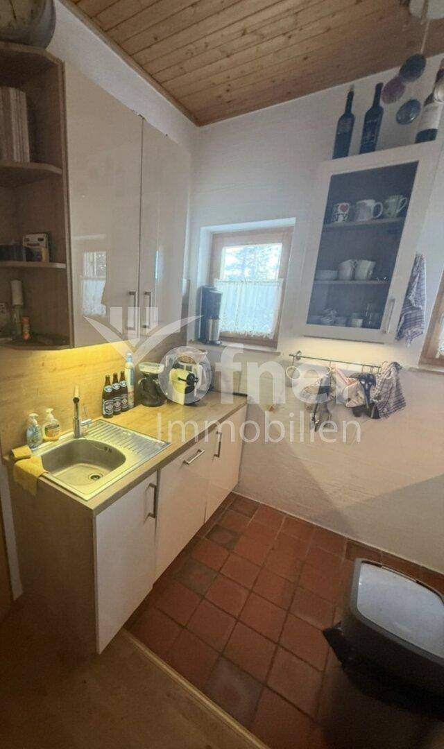 Kleine Küche mit weißen Schränken, Holztheke und Terrakotta-Fliesenboden, mit Blick nach draußen.