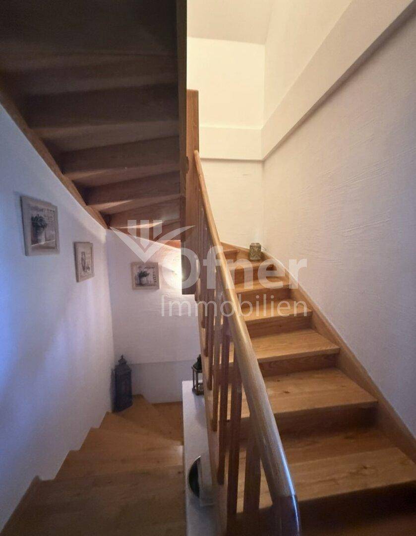 Rustikale Holztreppe mit Holzgeländer und weiß gestrichenen Wänden, die die Etagen verbindet.