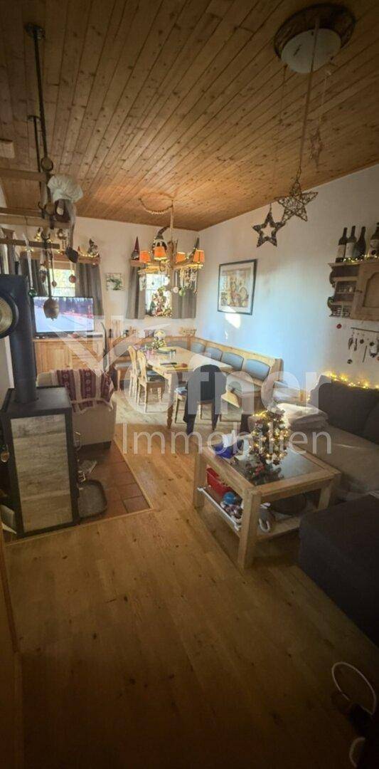 Geräumiger Wohn-Essbereich mit Holzboden, Holzdecke und einem Kaminofen als zentrale Wärmequelle.