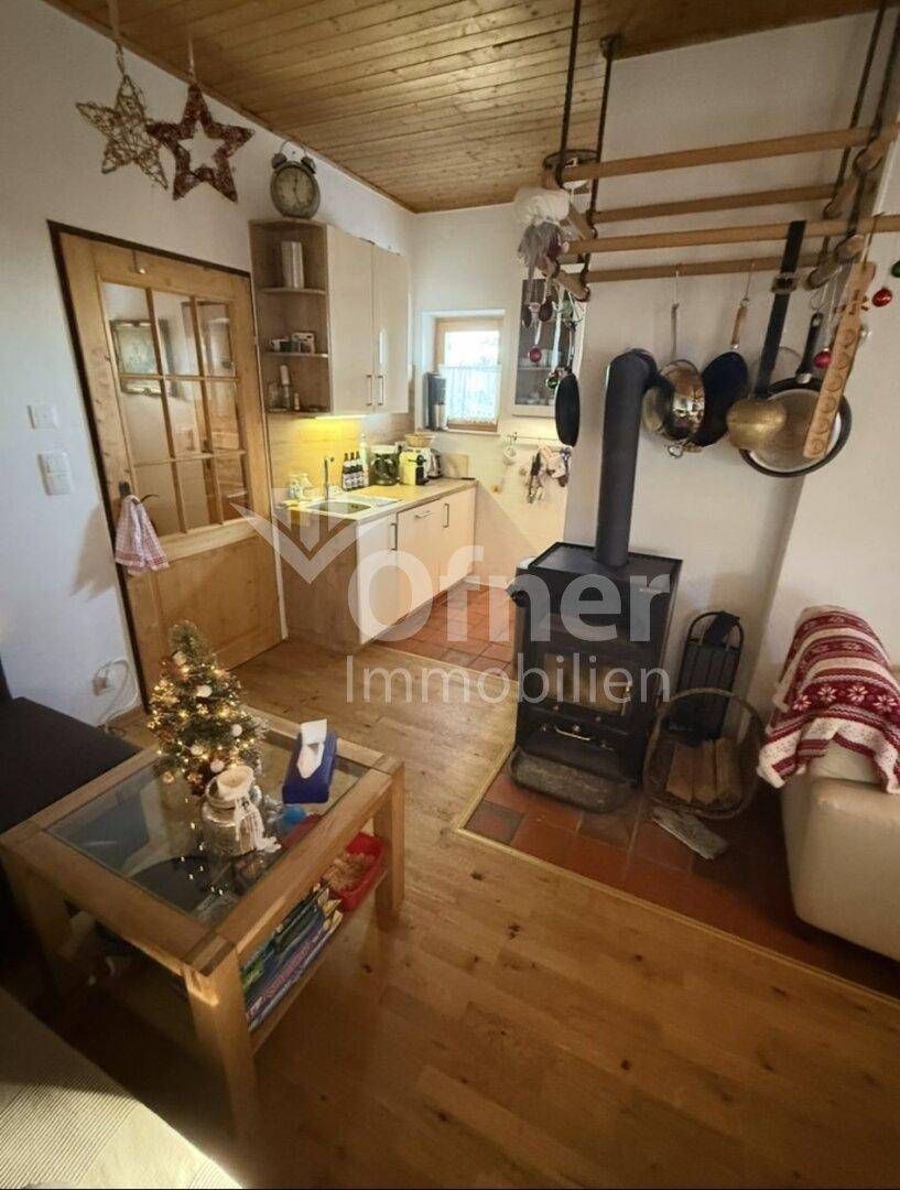 Gemütlicher Wohnbereich mit Holzboden, Kaminofen und Blick auf die angrenzende Küche.