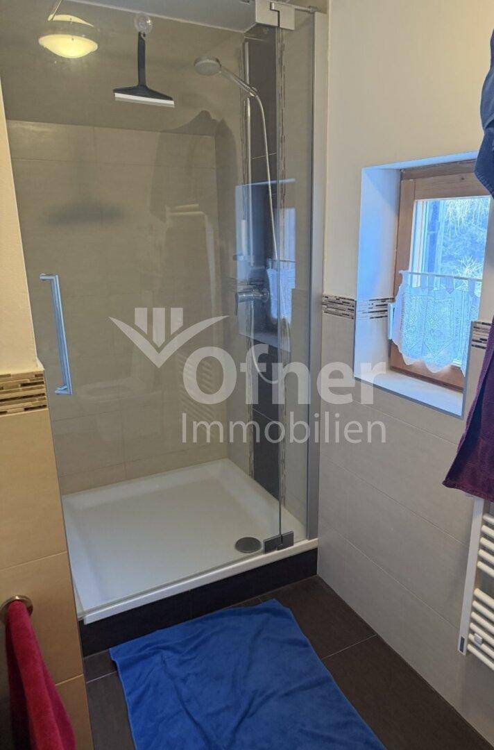 Badezimmer mit Duschkabine, beigefarbenen Fliesen und einem Fenster für natürliche Belüftung.