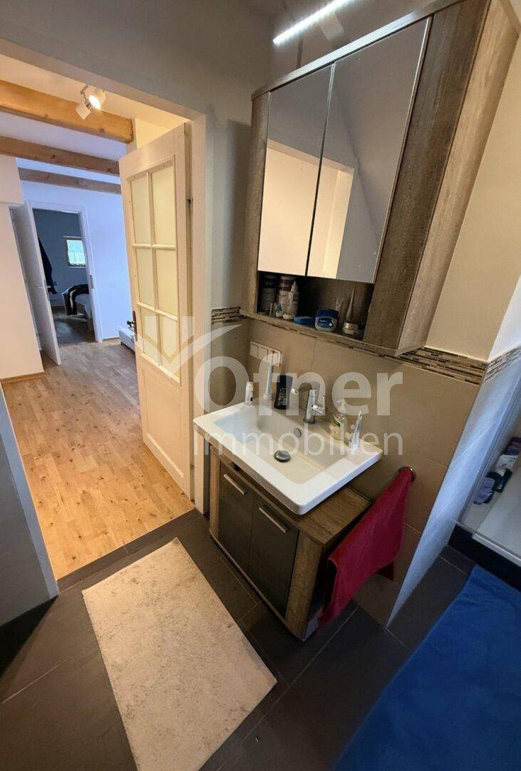 Badezimmer mit modernem Waschbeckenunterschrank und Spiegelschrank, mit Blick in den Flur.