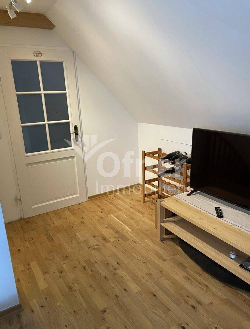 Gemütlicher Raum unter der Dachschräge mit Holzboden, Fernseher und Weinregal.