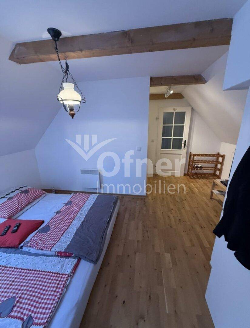Schlafzimmer unter der Dachschräge mit Holzboden, Holzbalken und einem Doppelbett.