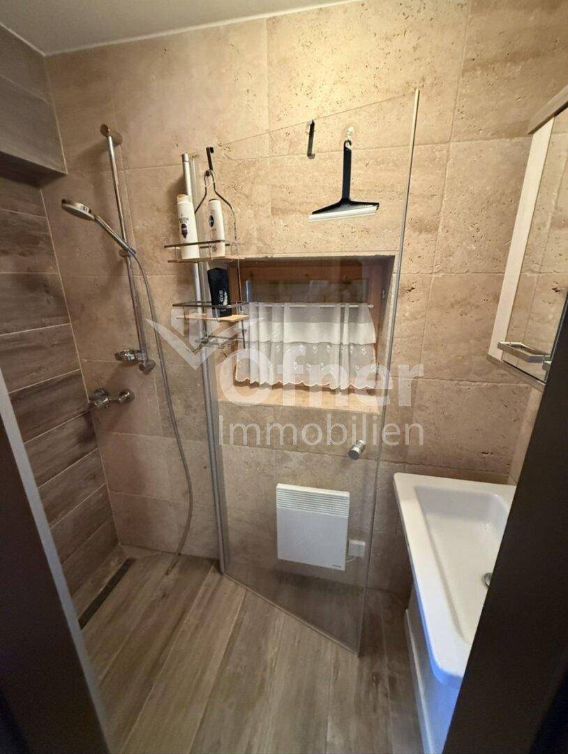 Modernes Badezimmer mit begehbarer Dusche, beigefarbenen Fliesen und einem kleinen Waschbecken.