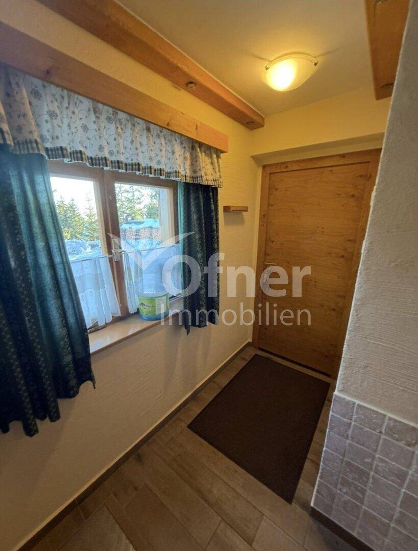 Heller Eingangsbereich mit Holzdecke, Fliesenboden und einem Fenster mit Blick ins Grüne.