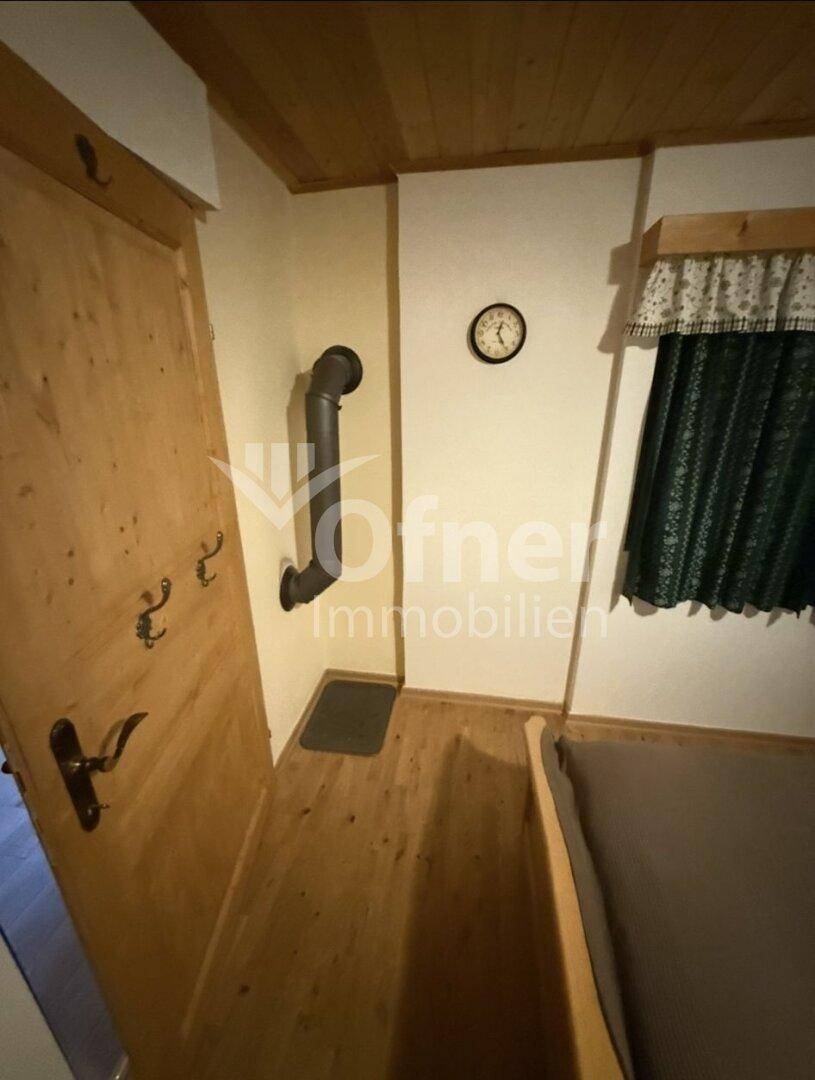 Gemütliches Schlafzimmer mit Holzboden, Fenster und einem Ofenrohr, das auf eine Heizquelle hindeutet.
