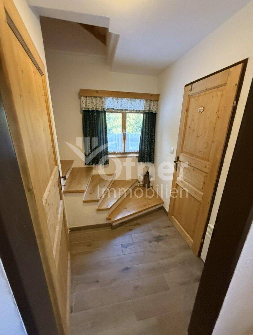 Eingangsbereich mit Holztüren, einem Fenster und Treppen, die zu den oberen Etagen führen.