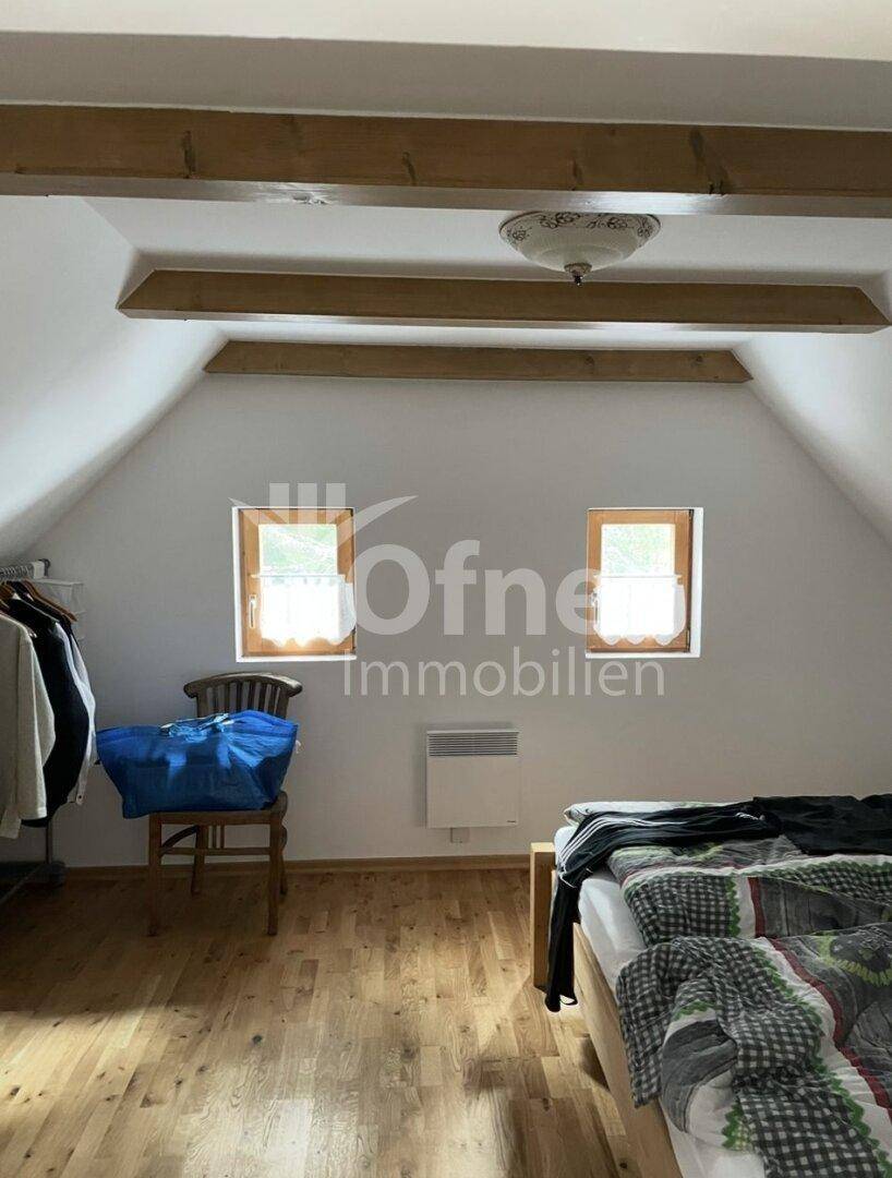 Helles Schlafzimmer unter der Dachschräge mit Holzboden, Holzbalken und zwei Fenstern.