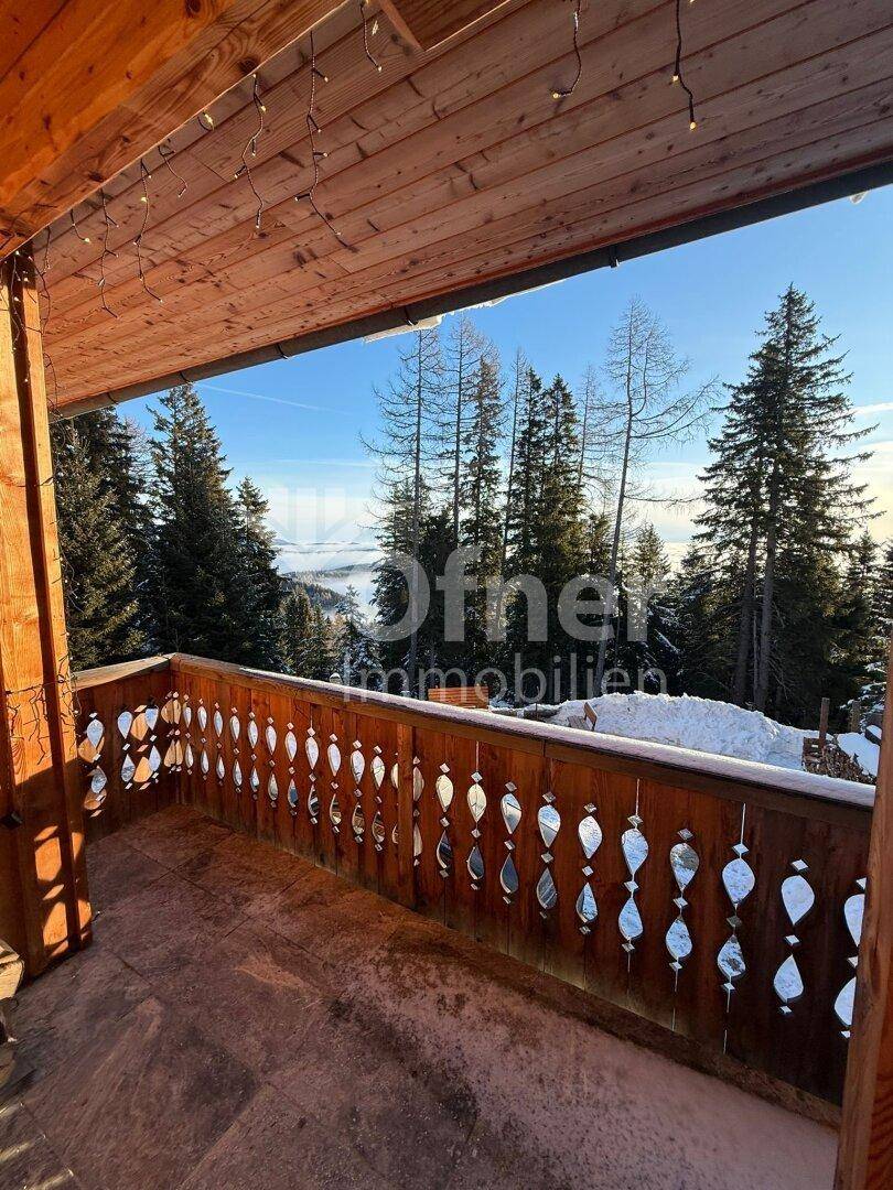 Sonniger Holzbalkon mit traditionellem Geländer und weitem Blick über die verschneite Landschaft.