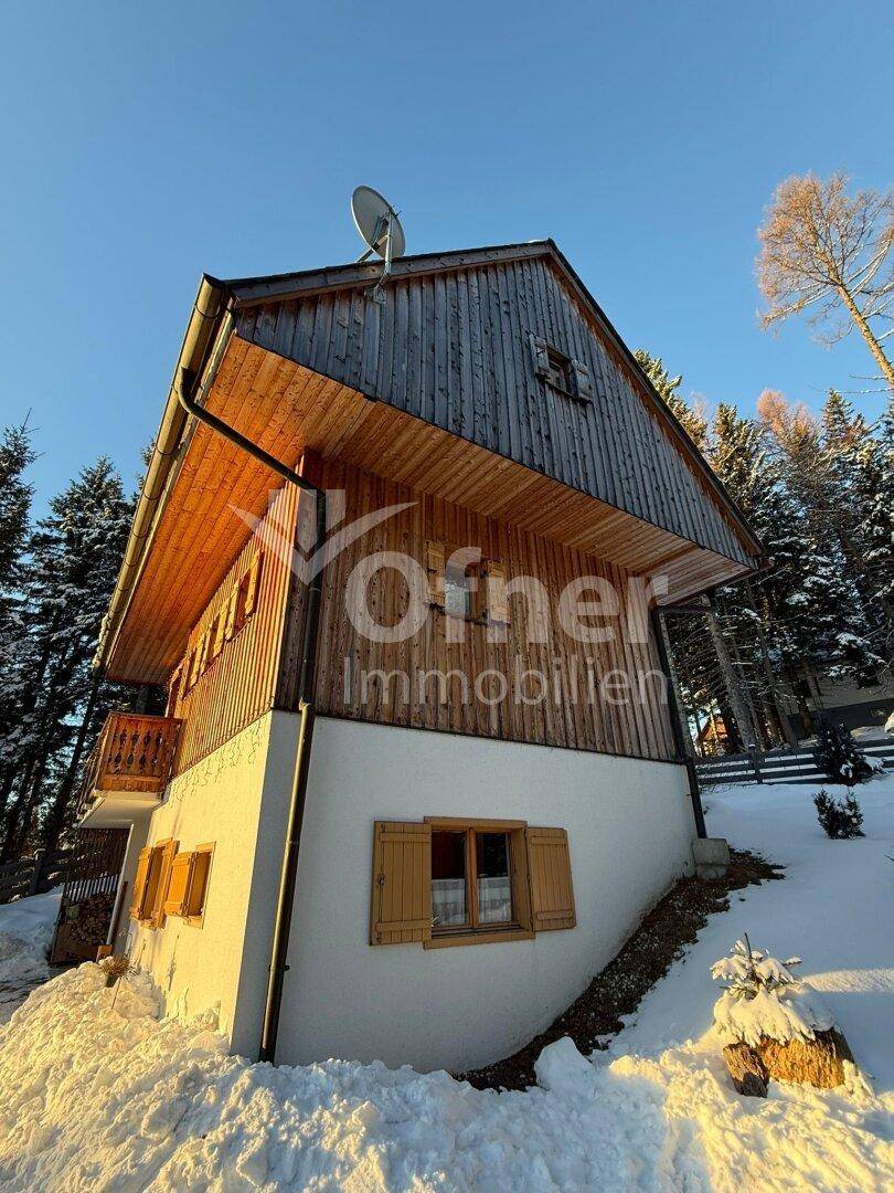 Rustikales Holzhaus mit schneebedeckter Umgebung und klarem Winterhimmel.