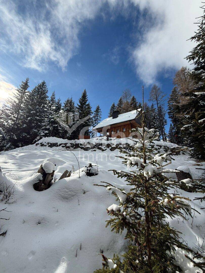 Gemütliches Holzhaus auf einem Hügel, eingebettet in eine tief verschneite Waldlandschaft.