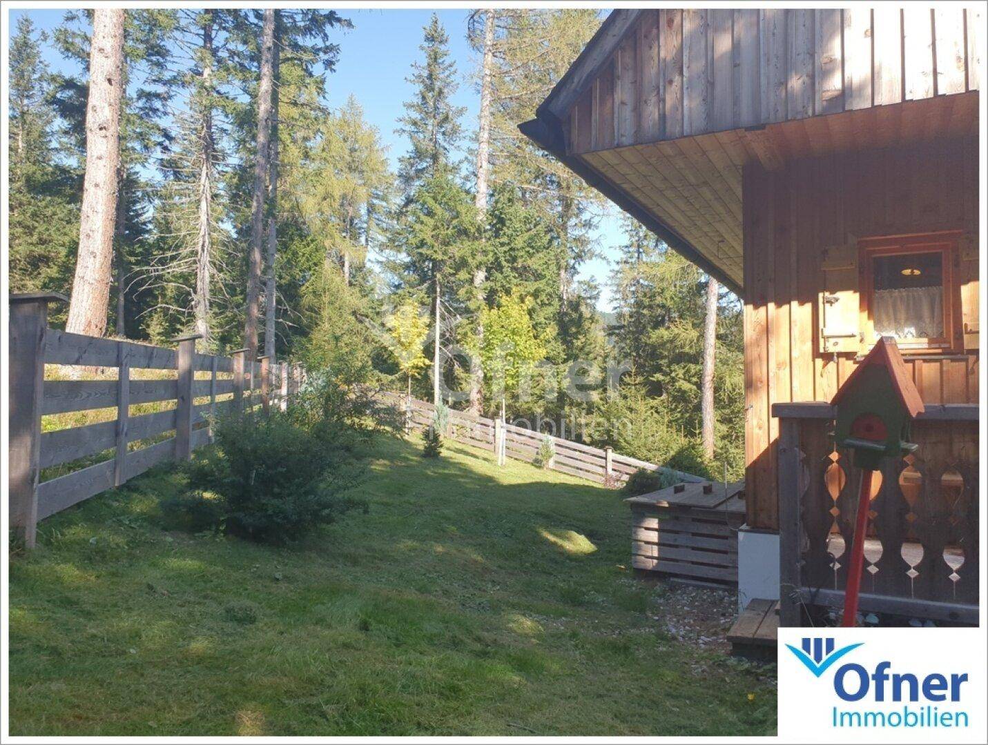 Gepflegter Gartenbereich mit Holzzaun und grüner Wiese, umgeben von hohen Bäumen.