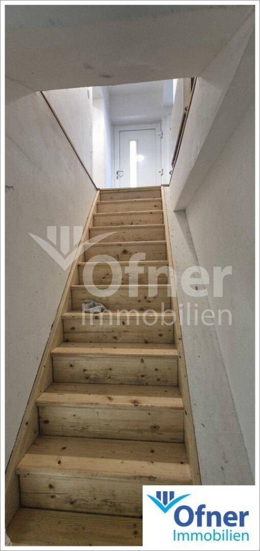 Holztreppe mit Blick nach oben zu einer Tür im Obergeschoss, die zu weiteren Räumen führt.