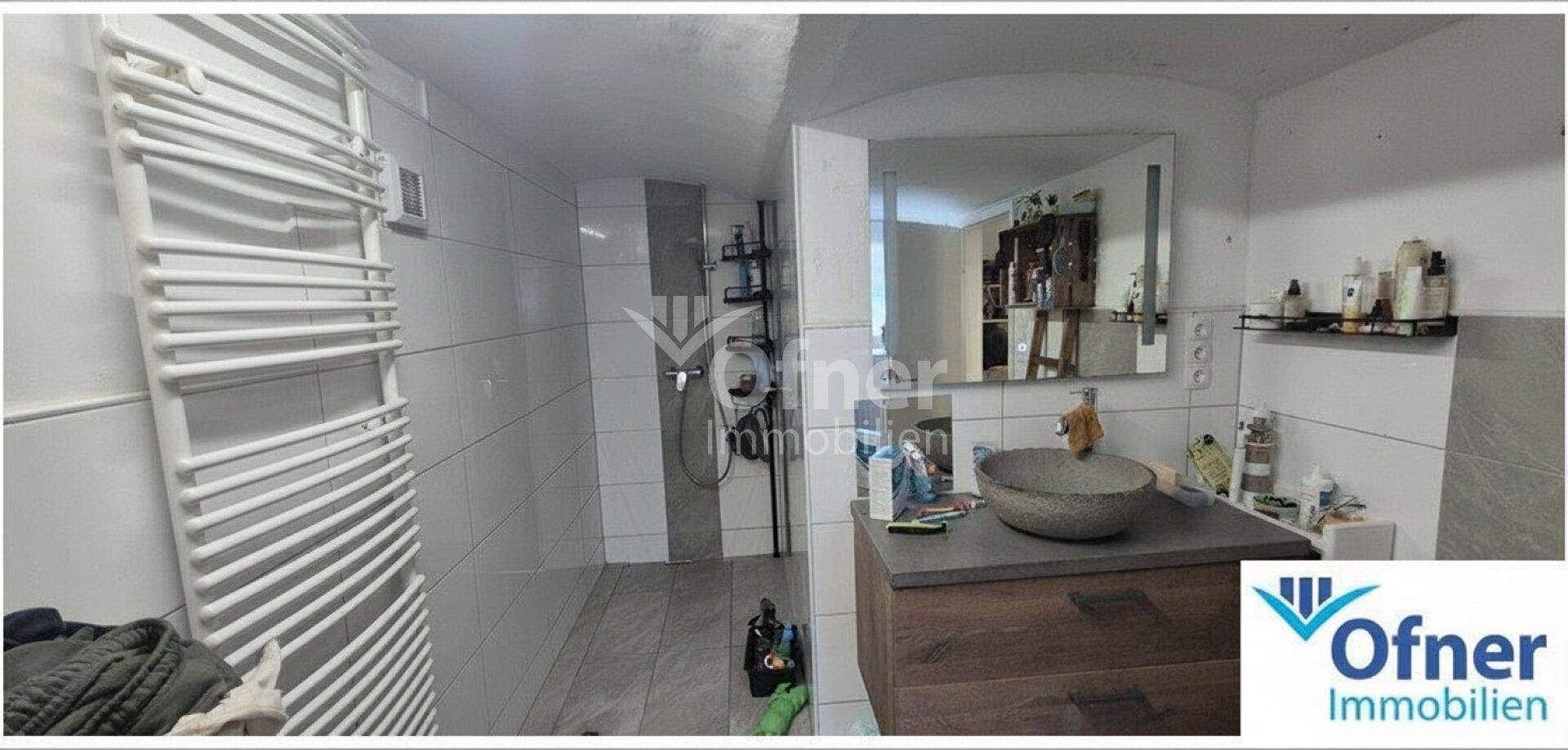Modern gefliestes Badezimmer mit Dusche, Waschbecken und beheiztem Handtuchhalter in Weißtönen.