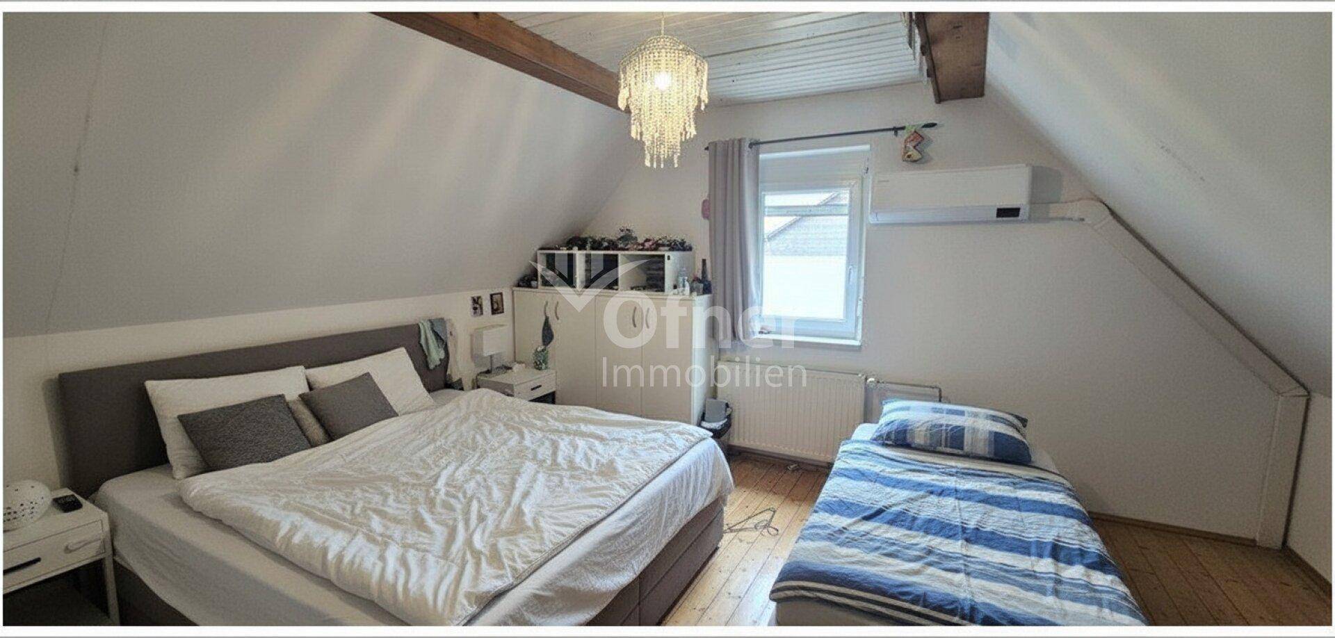 Helles Schlafzimmer im Dachgeschoss mit Holzbalken, Doppelbett, Einzelbett und Klimaanlage.