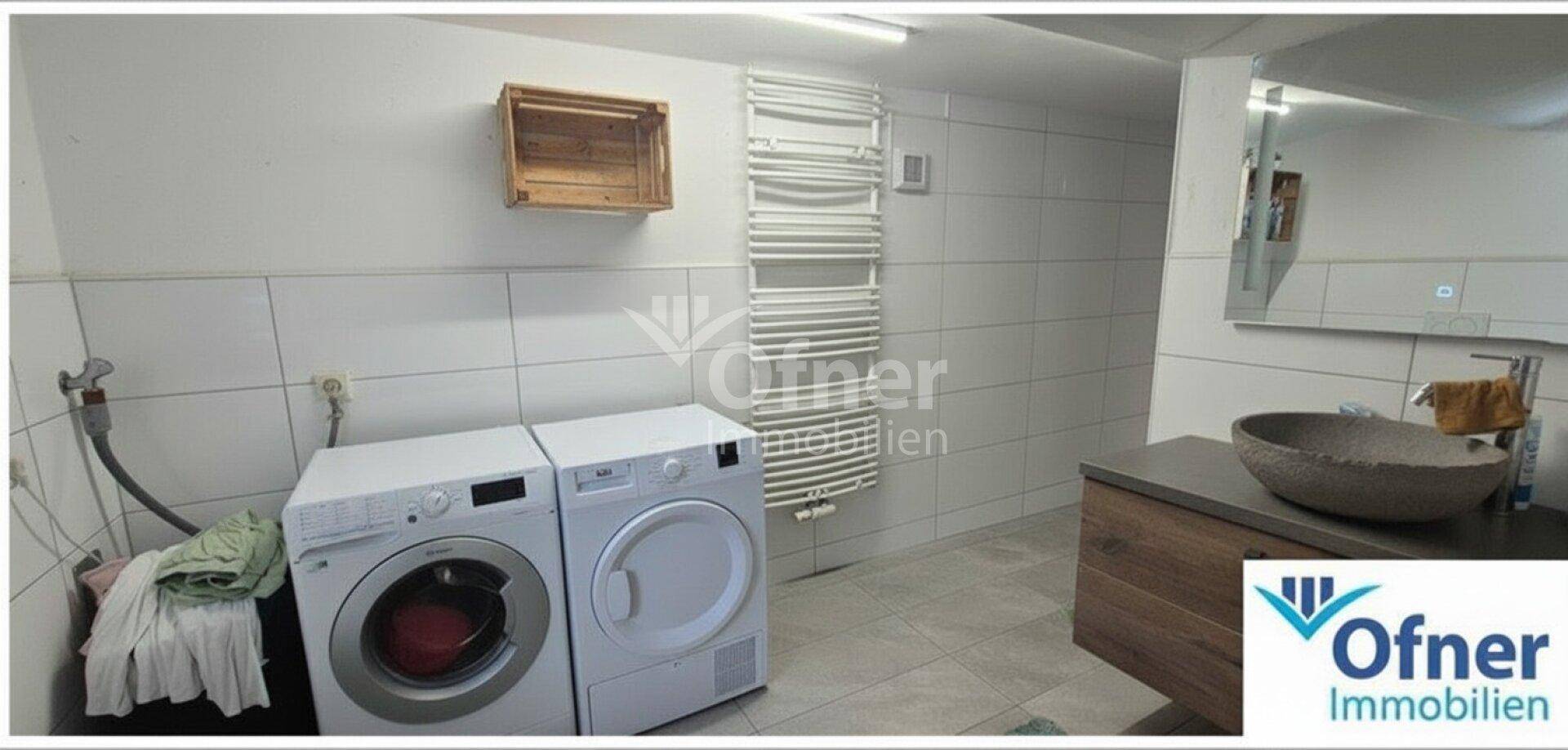 Badezimmer mit Waschmaschine, Trockner, Waschbecken und beheiztem Handtuchhalter, praktisch eingerichtet.