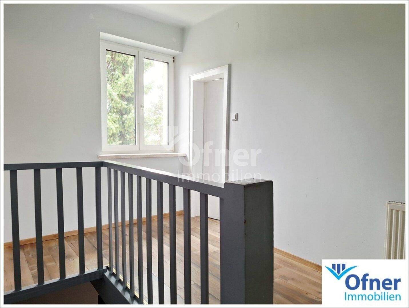 Heller Flur im Obergeschoss mit Holzboden, Fenster und Blick ins Grüne.