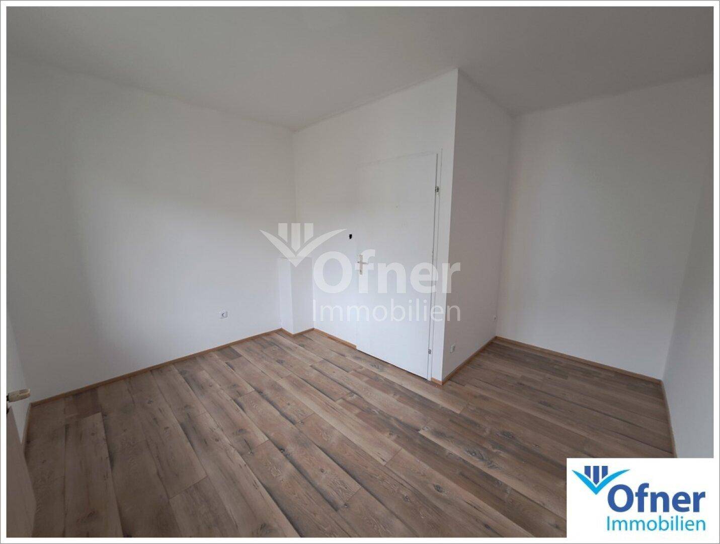 Leeres Zimmer mit Holzboden und weiß gestrichenen Wänden, bereit zur individuellen Gestaltung.
