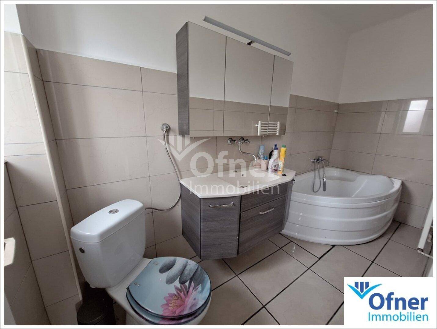Badezimmer mit Eckbadewanne, WC und Waschbeckenunterschrank, in neutralen Farbtönen gehalten.