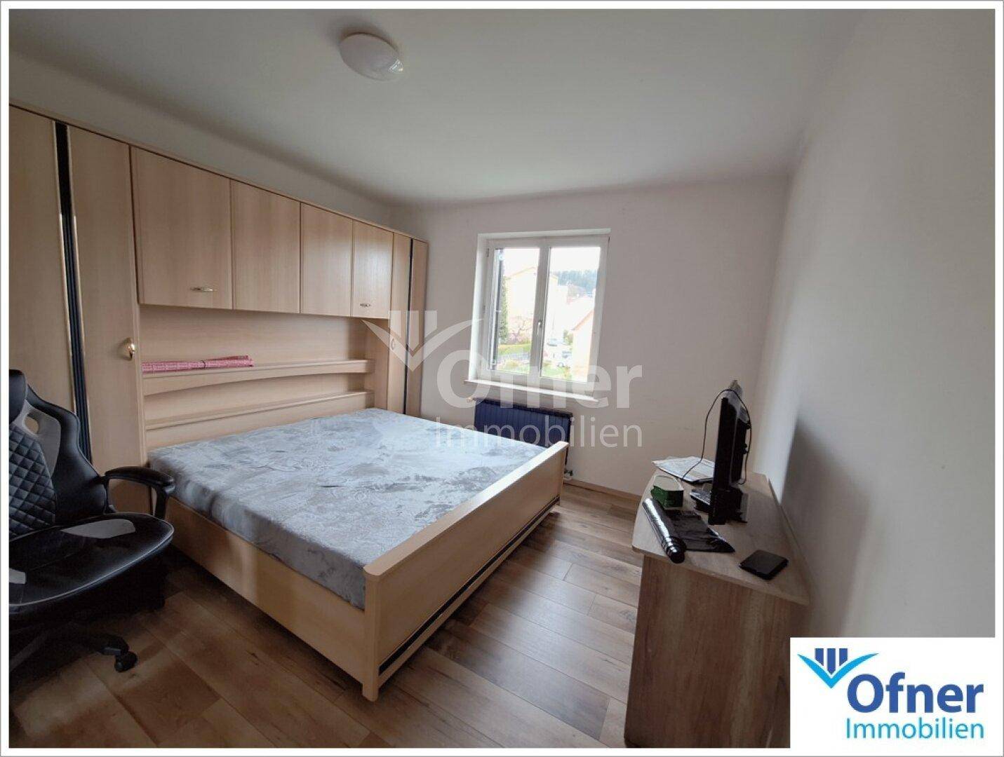 Schlafzimmer mit Holzboden, Einbauschränken und einem Fenster, das Tageslicht spendet.