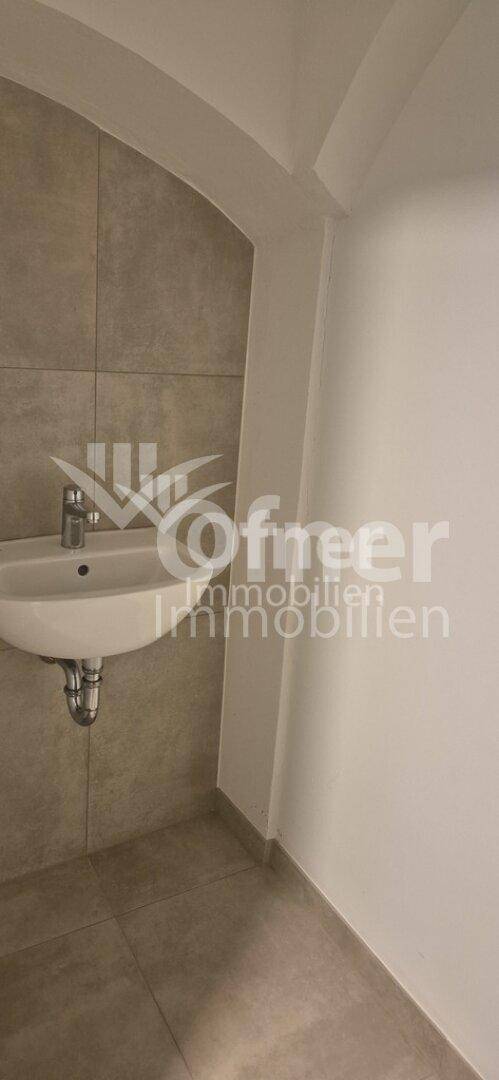 Modern gefliestes WC mit Waschbecken und Wandfliesen in neutralem Farbton.