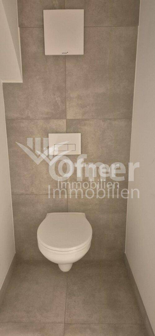 Modern gefliestes WC mit Wand-WC und Spülkasten in einem schlichten Design.