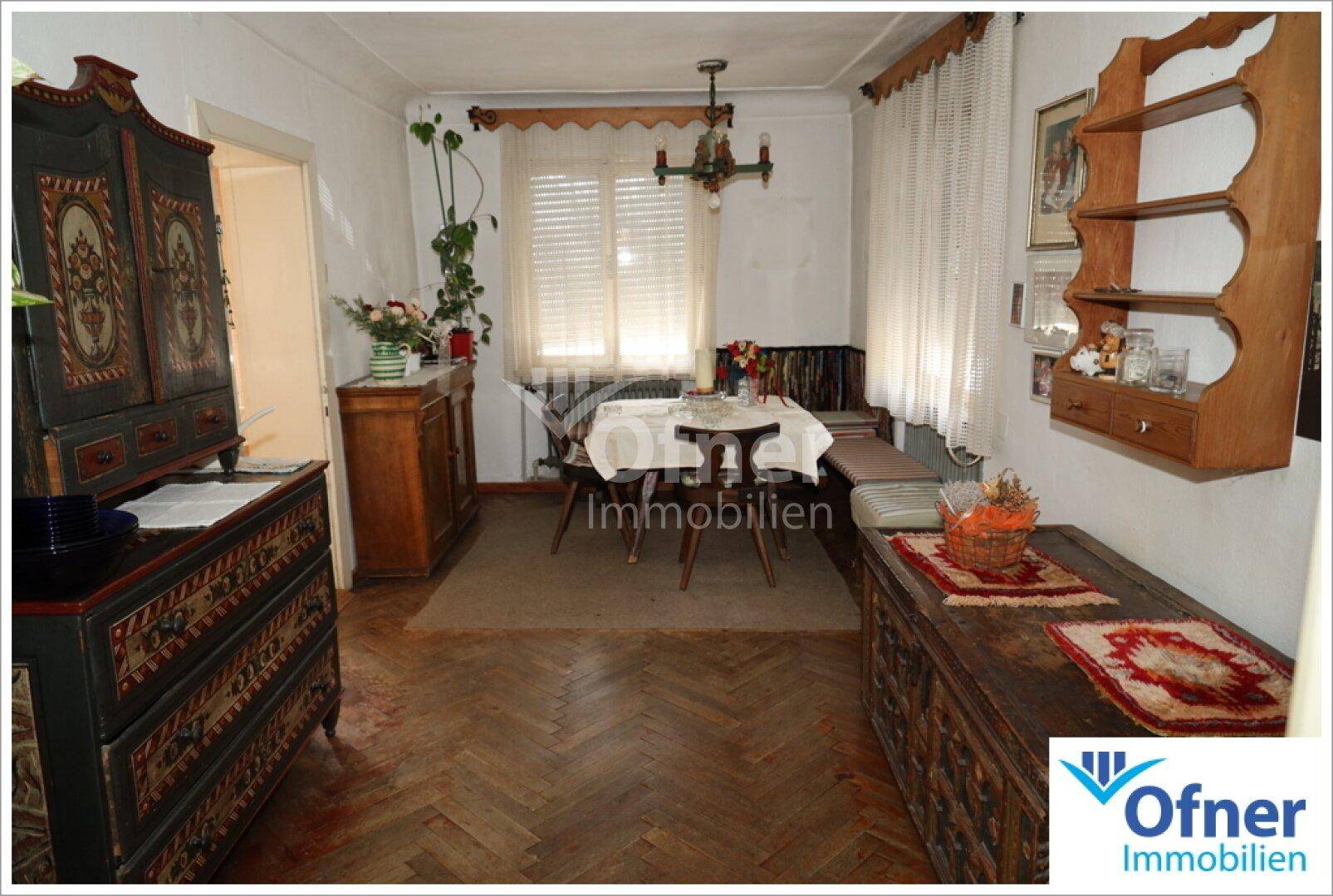 Gemütliches Esszimmer mit Holzboden, traditionellen Möbeln und einem Kachelofen im Hintergrund.