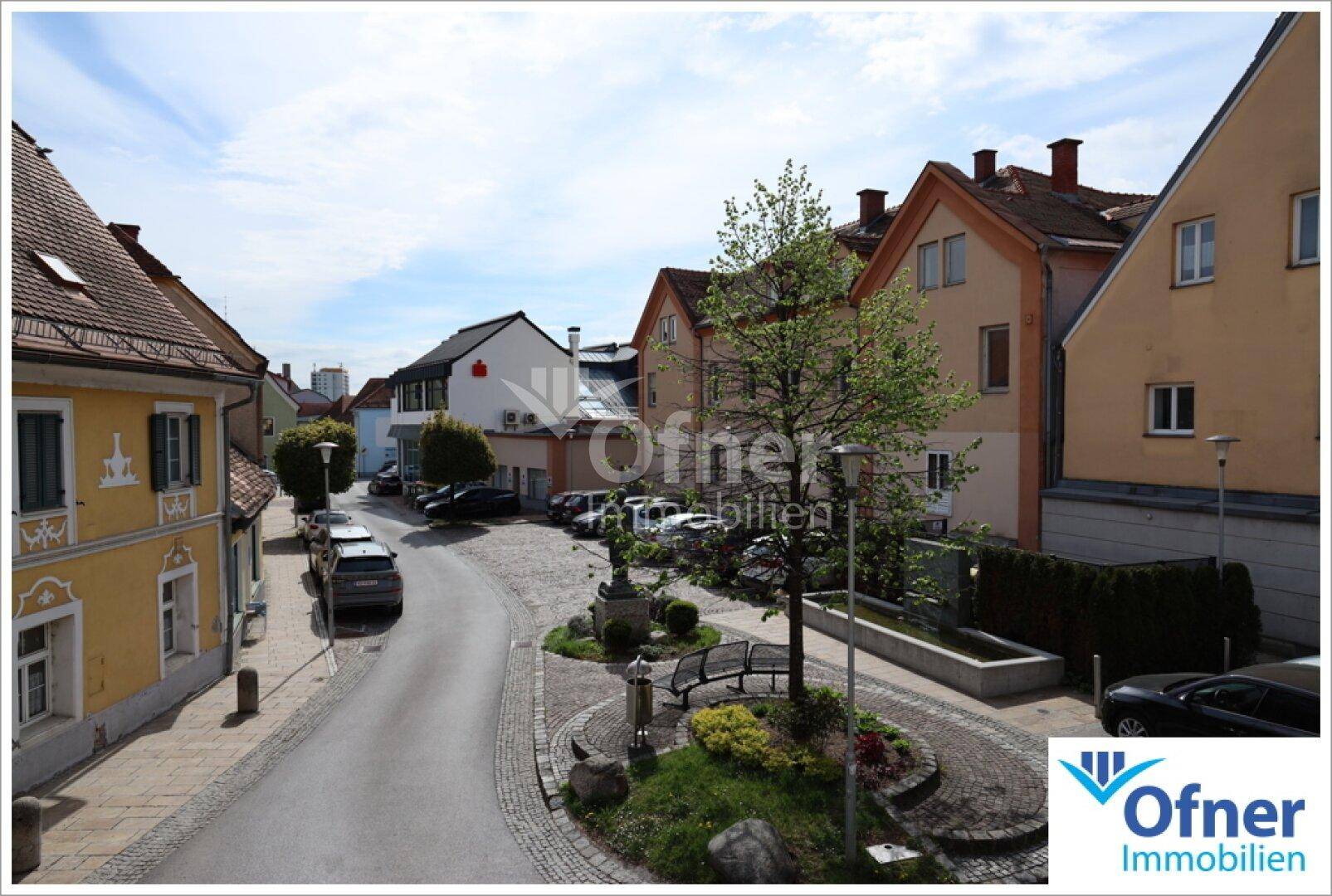 Blick auf eine ruhige Wohnstraße mit geparkten Autos und traditionellen Häusern unter blauem Himmel.
