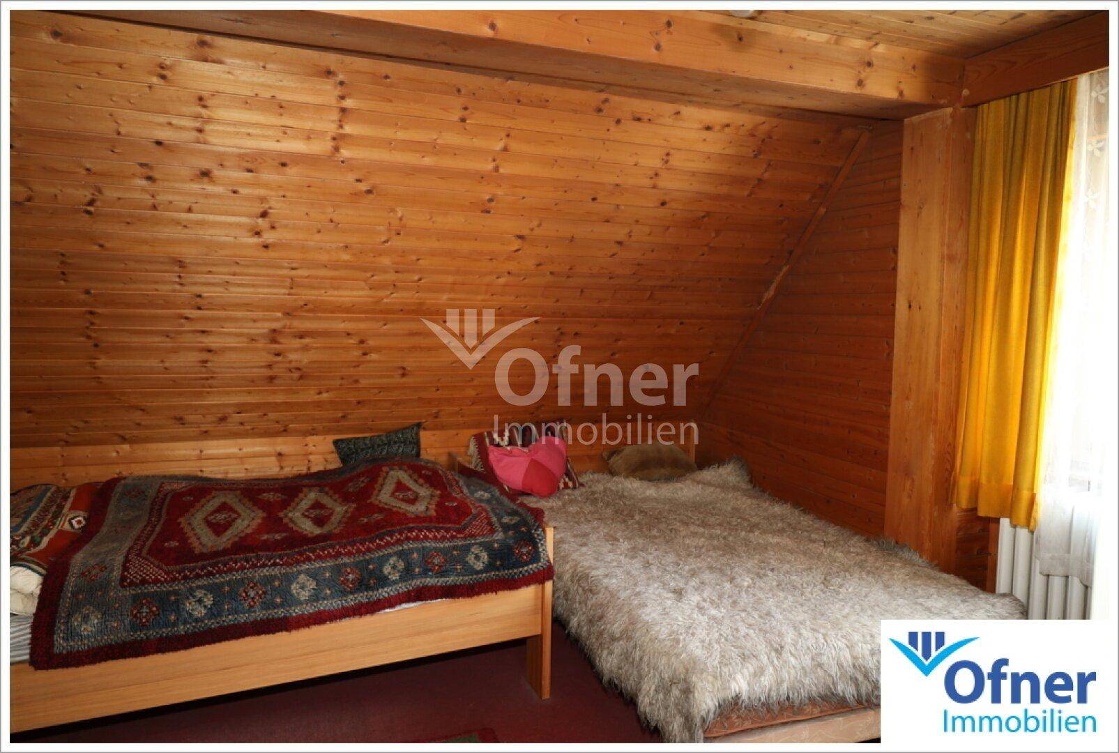 Schlafzimmer im Dachgeschoss mit Holzverkleidung an Wänden und Decke sowie schrägen Dachschrägen.