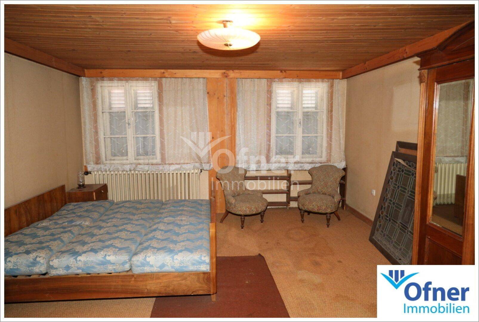 Schlafzimmer mit Doppelbett, Teppichboden und Holzdecke, beleuchtet durch zwei Fenster.