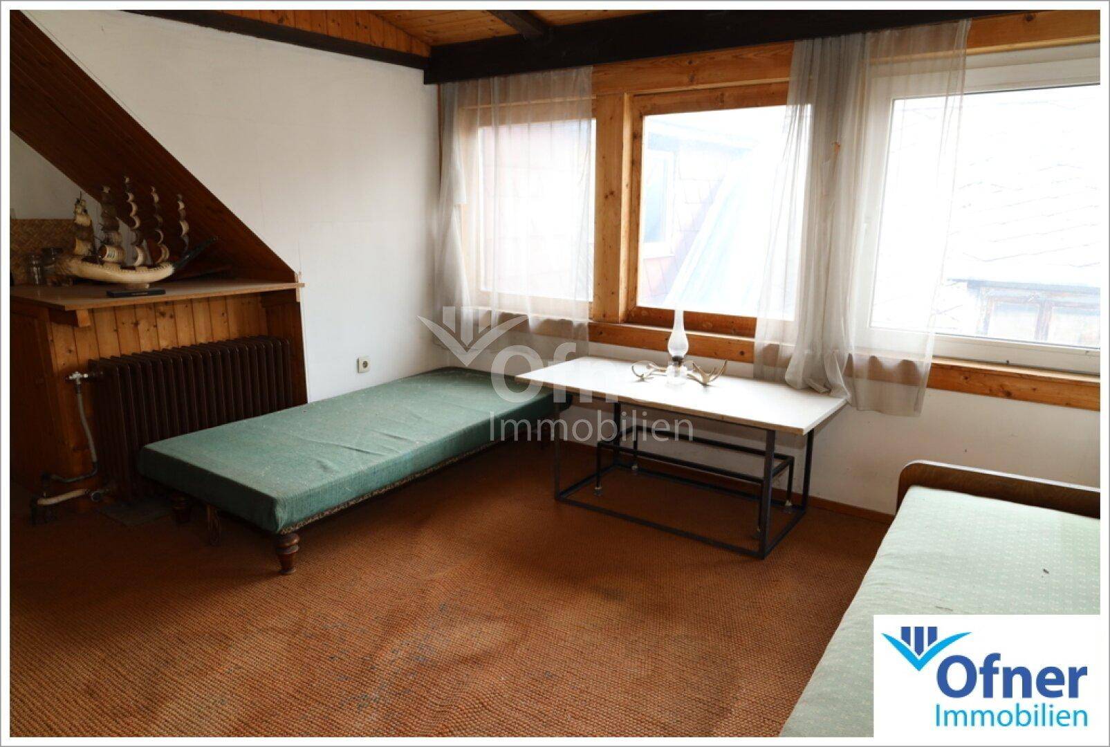Schlafzimmer im Dachgeschoss mit schrägen Wänden, Holzdecke und zwei Einzelbetten, hell beleuchtet.