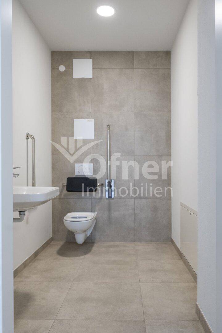Barrierefreies WC mit Haltegriffen, Wand-WC und Waschbecken in modernem Design.