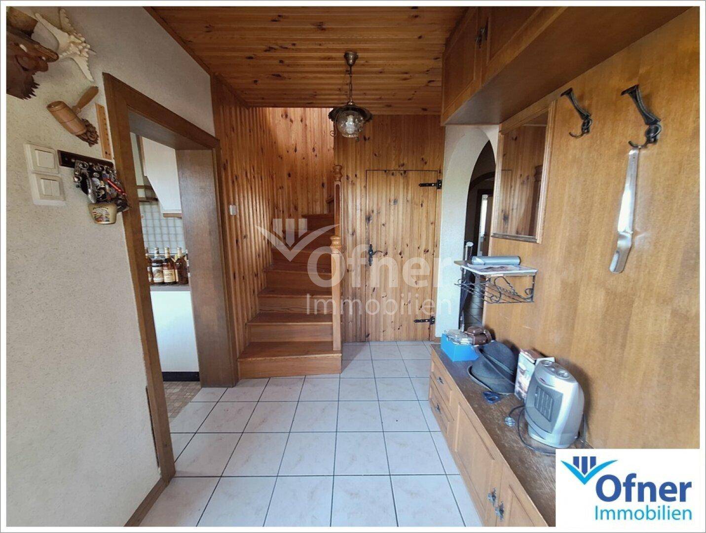 Eingangsbereich mit Holzvertäfelung, Fliesenboden und Treppe zum Obergeschoss.