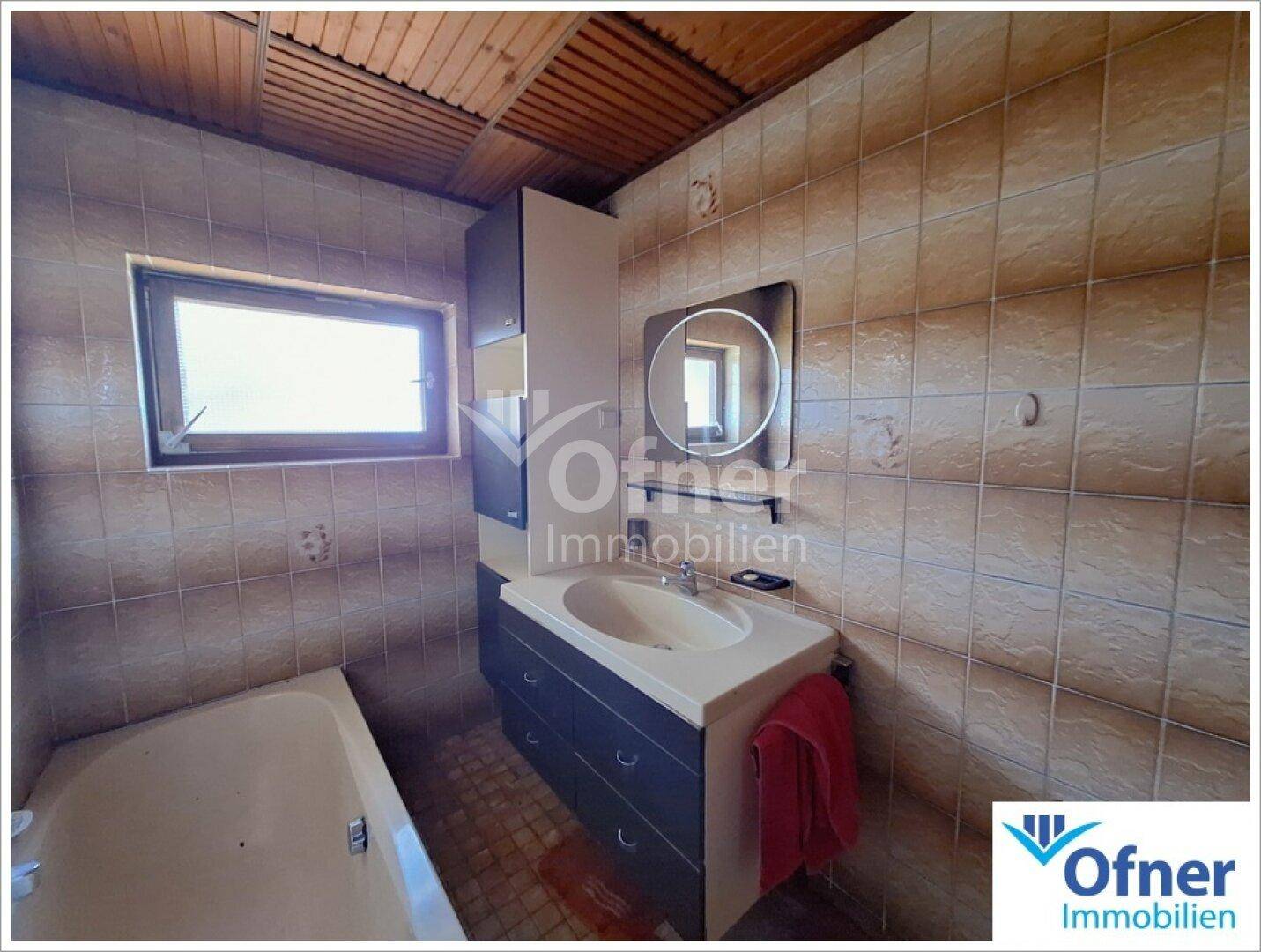 Badezimmer mit Badewanne, Waschbecken und braunen Fliesen an Wänden und Boden.