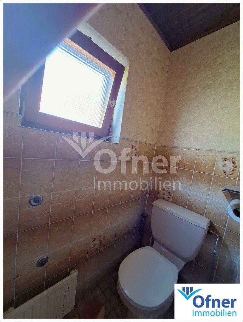 Separate Toilette mit Fenster und braunen Wandfliesen.