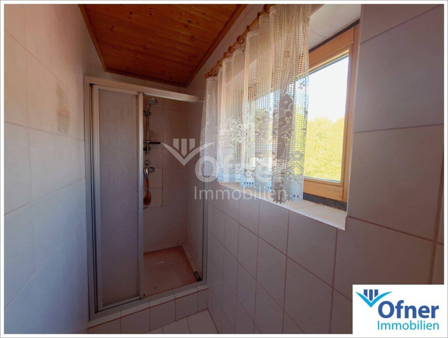 Duschbereich im Badezimmer mit Fenster und weißen Wandfliesen.