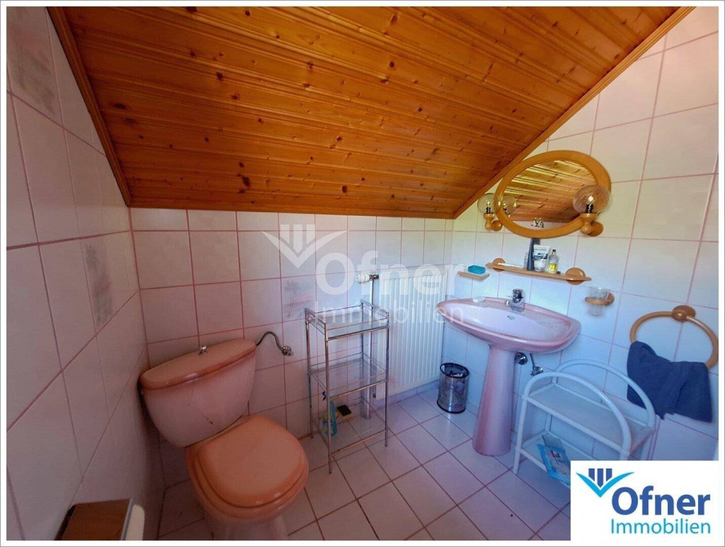 Badezimmer mit rosa Waschbecken, Toilette und weißen Fliesen an Wänden und Boden.
