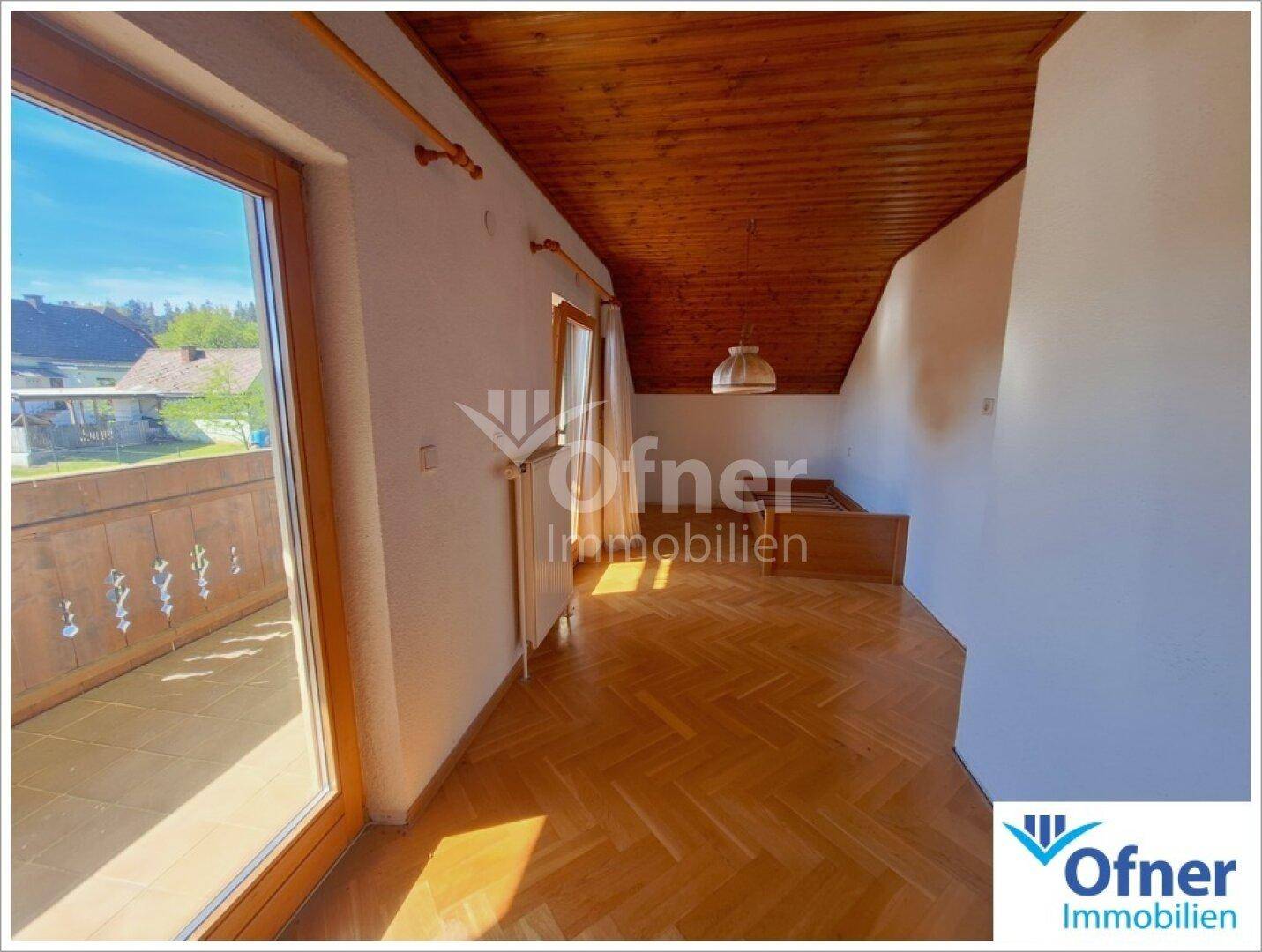 Heller Raum mit Parkettboden, Holzdecke und Zugang zu einem Balkon.