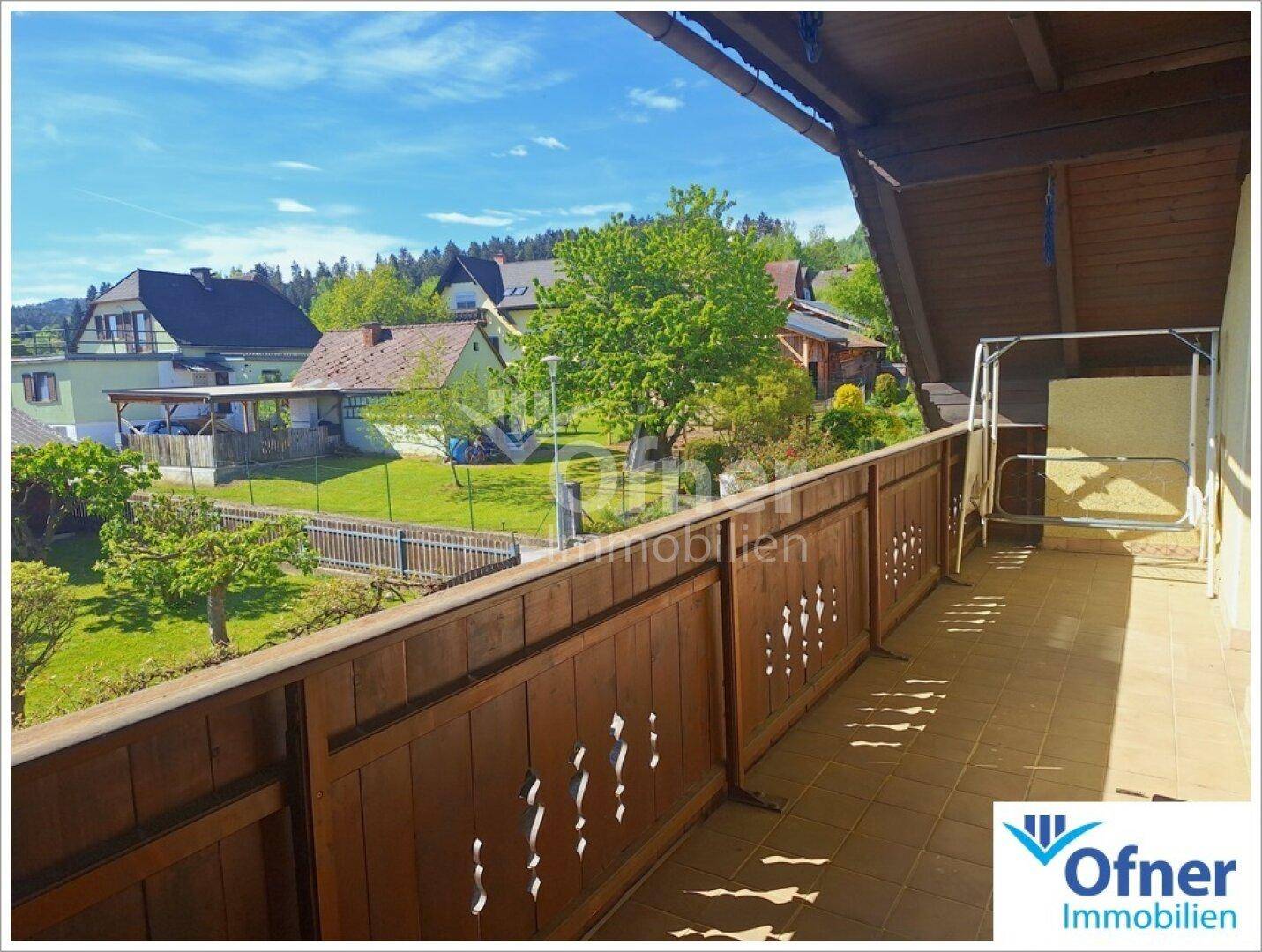 Geräumiger Balkon mit Fliesenboden und Holzbalkongeländer, bietet Blick ins Grüne.