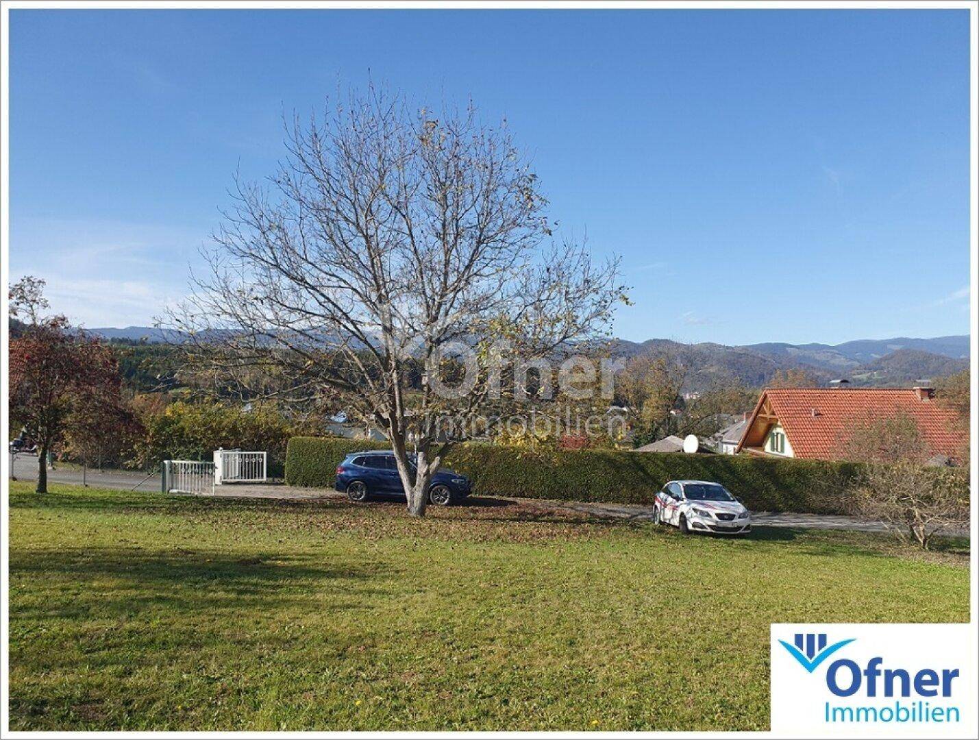 Weitläufige Landschaft mit Blick auf sanfte Hügel und Bäume, zwei Autos parken am Straßenrand.