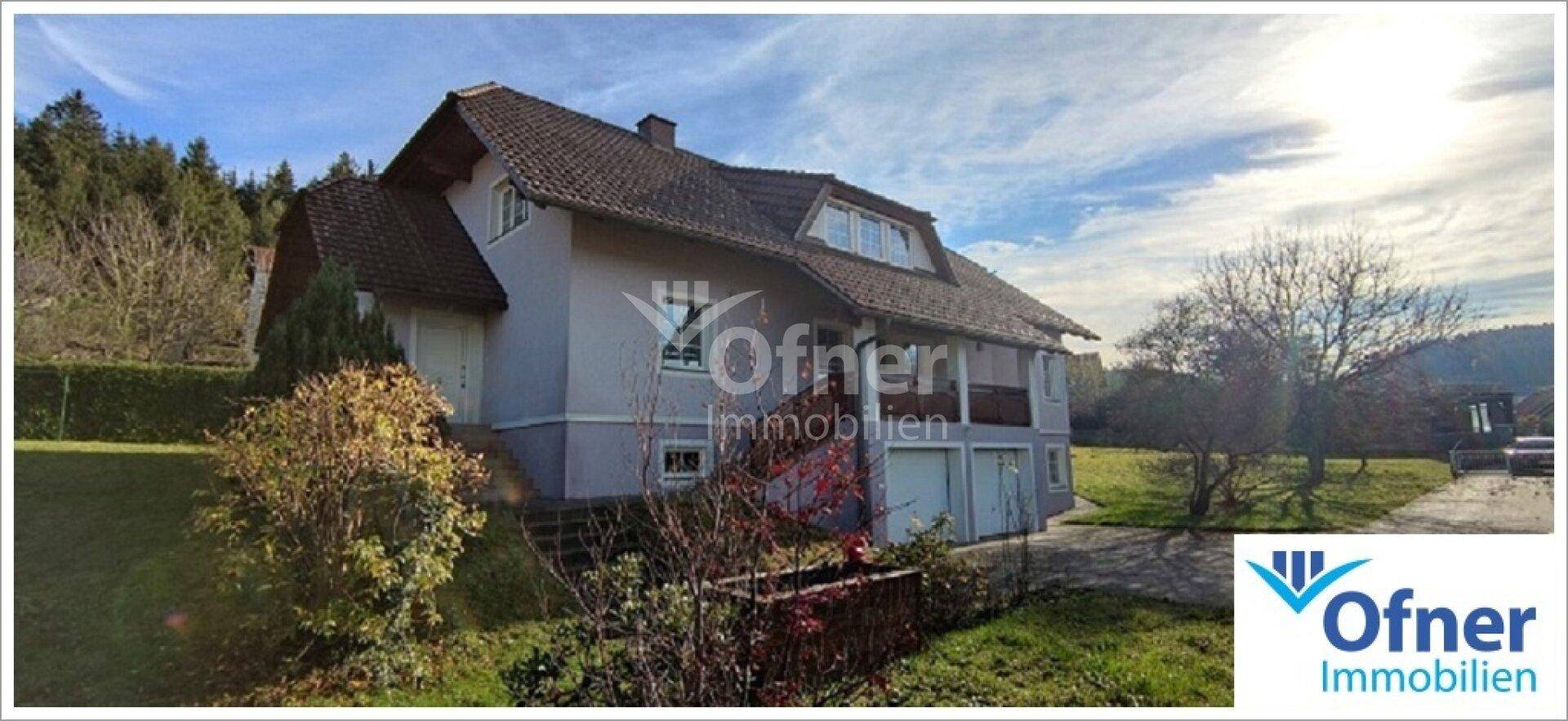 Das Einfamilienhaus von der Seite, mit Doppelgarage und Zugang zum Garten, umgeben von Bäumen.